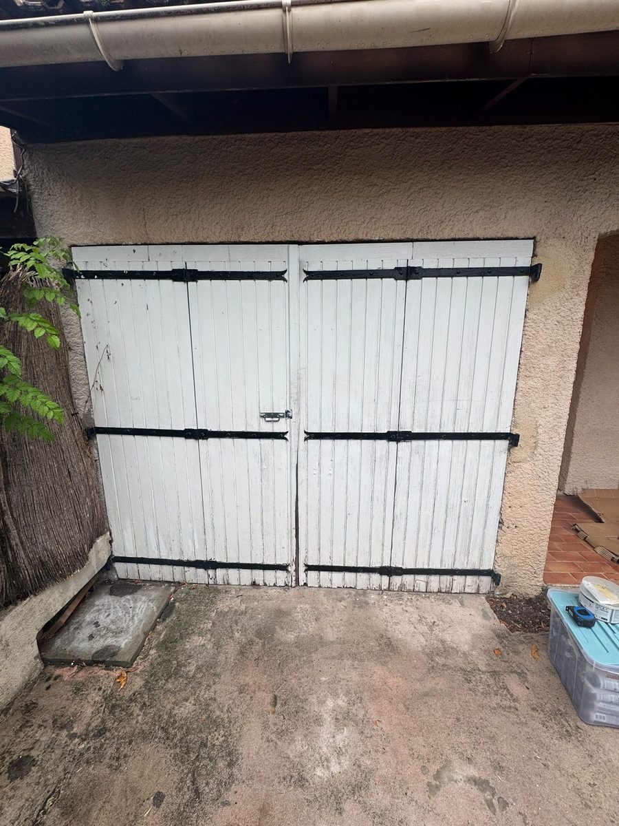 Ancienne porte de garage battante en bois peint blanc avec pentures noires